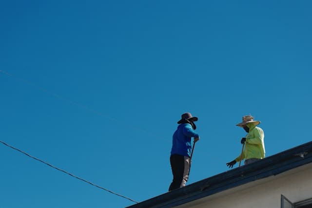 Two workers on a roof under a clear blue sky